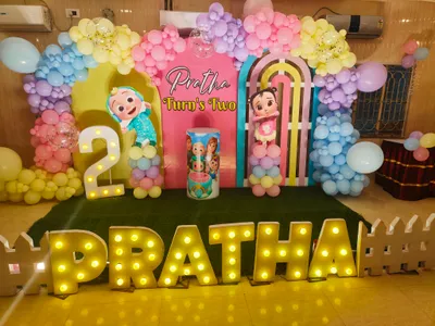 Birthday party stage decoration in Behala, Kolkata with pastel balloon arch, cartoon cutouts, illuminated name letters, and number 2 for girl's second birthday