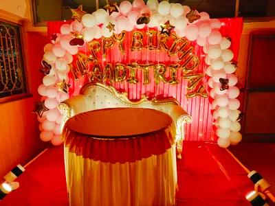 Birthday party stage decoration in Behala, Kolkata with golden sofa, round table, pink and white balloon arch, and "Happy Birthday Aadritri" foil letters