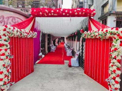 Entrance decorated with red and white floral garlands and drapes leading to banquet hall seating arrangement for wedding event in Behala, Kolkata