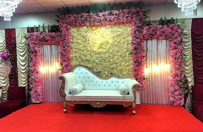 Elegant wedding stage decoration with white and pink floral backdrop, vintage sofa, and draped curtains in banquet hall, Behala, Kolkata