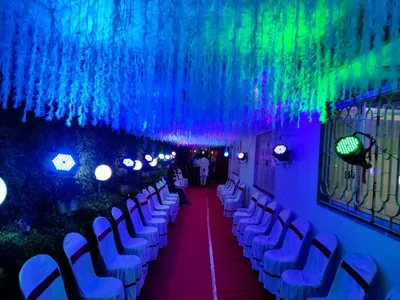 Banquet hall corridor decorated with white floral ceiling, vibrant blue and green LED lighting, and red carpet seating for wedding event in Behala, Kolkata.