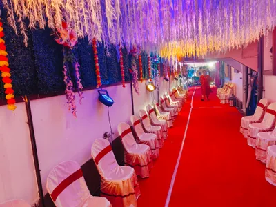 Banquet hall corridor decorated with white hanging floral arrangements, colorful marigold garlands, and rows of white chairs with red sashes for wedding event in Behala, Kolkata