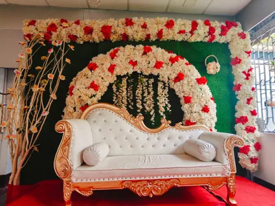 Elegant wedding stage setup with white and red floral arch and vintage gold sofa on red carpet in Kolkata event decoration.