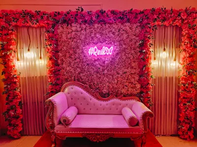 Pink floral wall backdrop with neon #Rini butterfly sign and vintage pink sofa for event decoration in Kolkata.